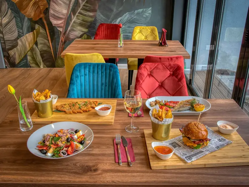 A restaurant table with a burger, salad, schnitzel and fish dishes beside colorful chairs